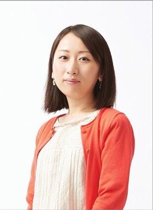 A waist-up picture of a woman with shoulder-length black hair and brown eyes, wearing a red cardigan and white blouse, looking at the camera from a slight angle.