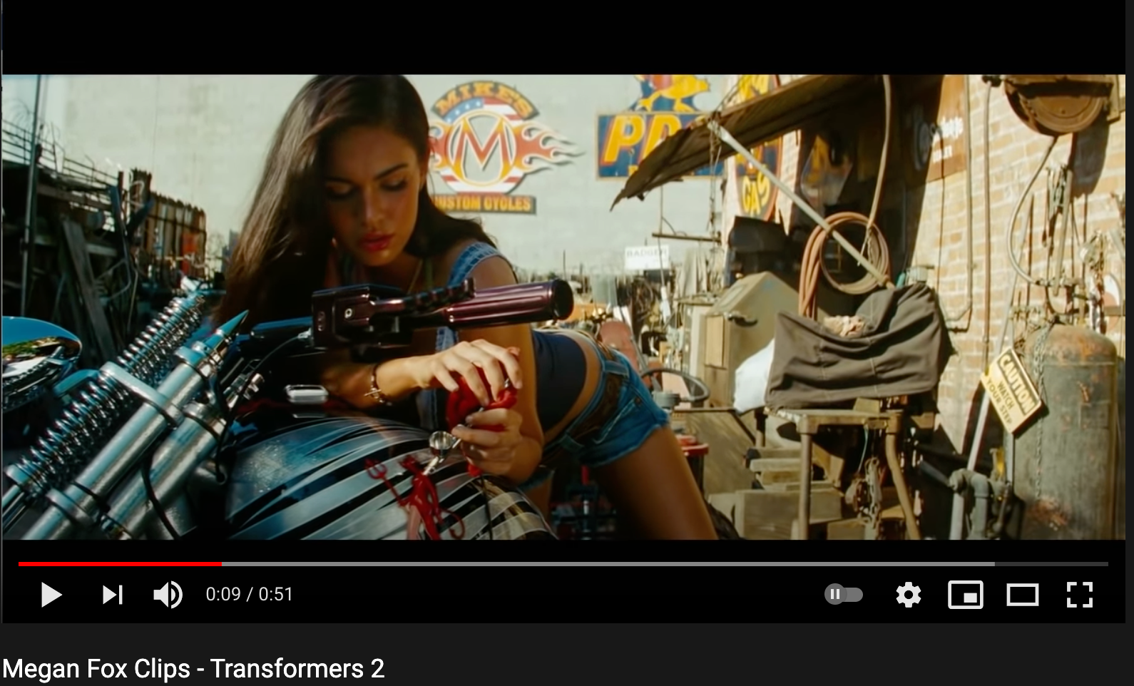 Screenshot of a youtube video of Megan Fox clips in which she is posed on a motorcycle, working on a decal