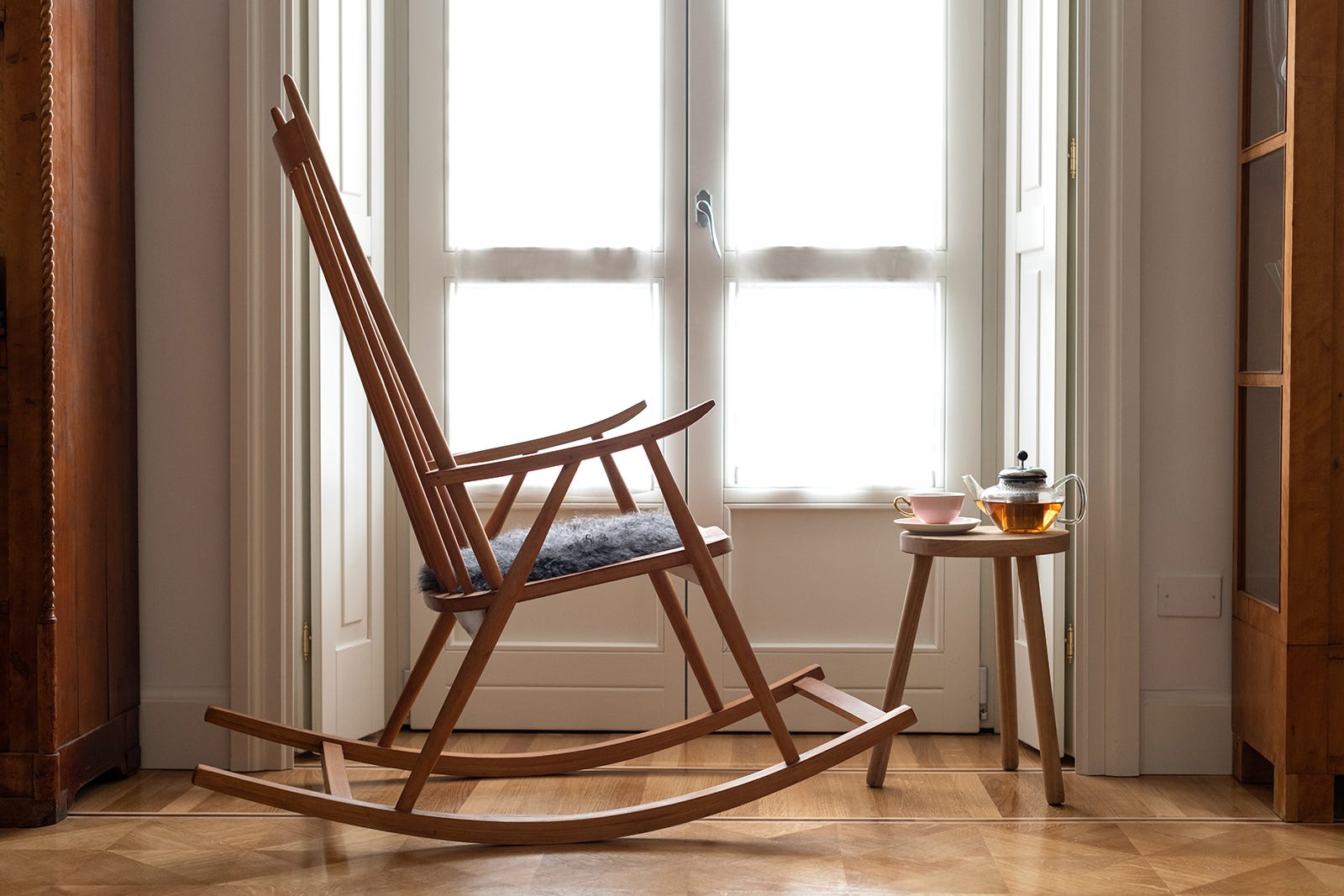Photo of a rocking chair in front of a window with a small table with tea on top.