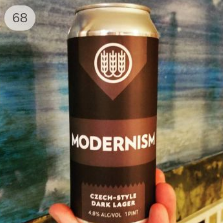 A back beer can stands in contrast to a piece of art behind it, the artwork depicts a tranquil blue sky