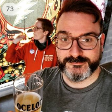 A man and a woman play darts at a brewery taproom, a grateful dead banner is in the background