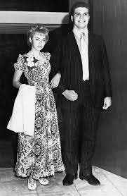 A young girl in a long dress and a flower pin posing with a boy in a dark suit