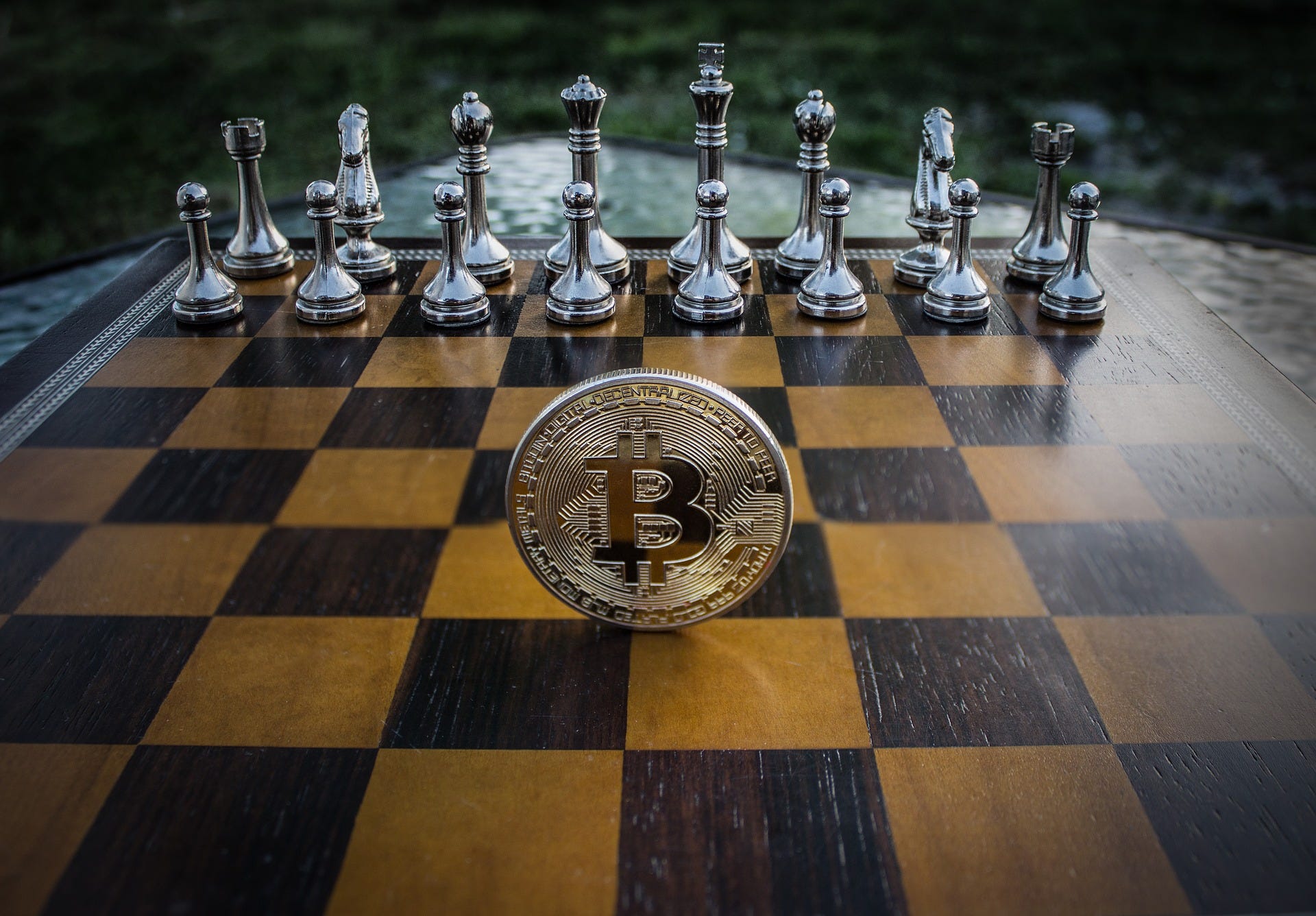 A metal coin with the Bitcoin logo standing on its edge in the middle of a chess board