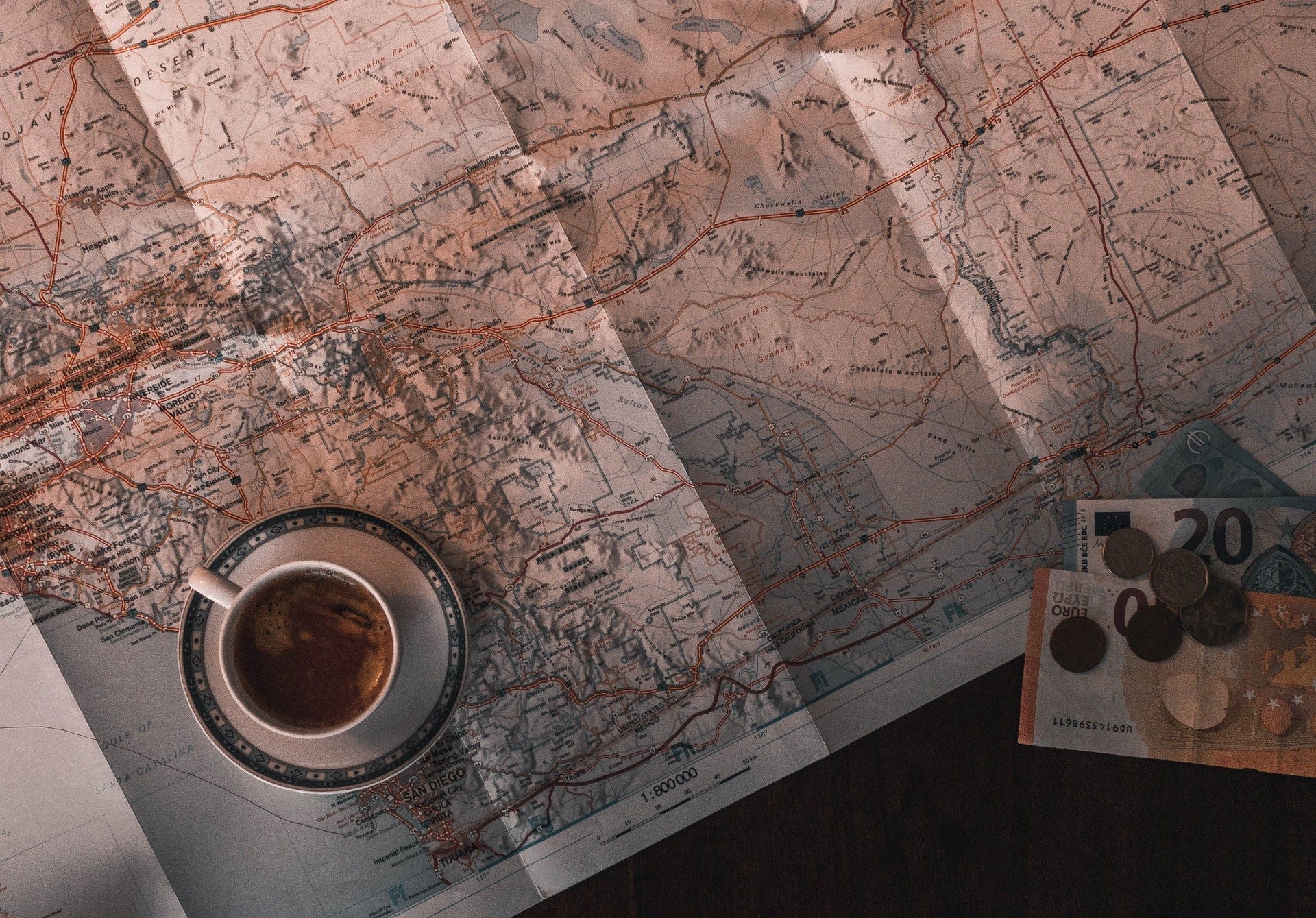 a map with a cup of coffee on it and euro banknotes and coins placed on a table