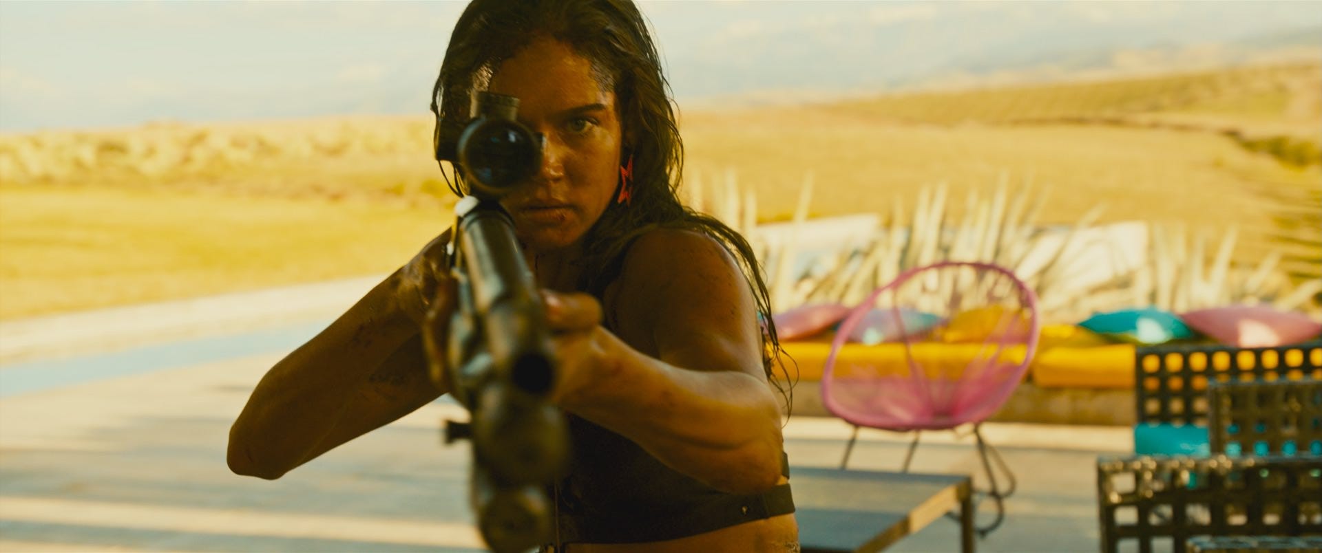 A woman is seen holding a rifle towards the viewer in a patio setting.