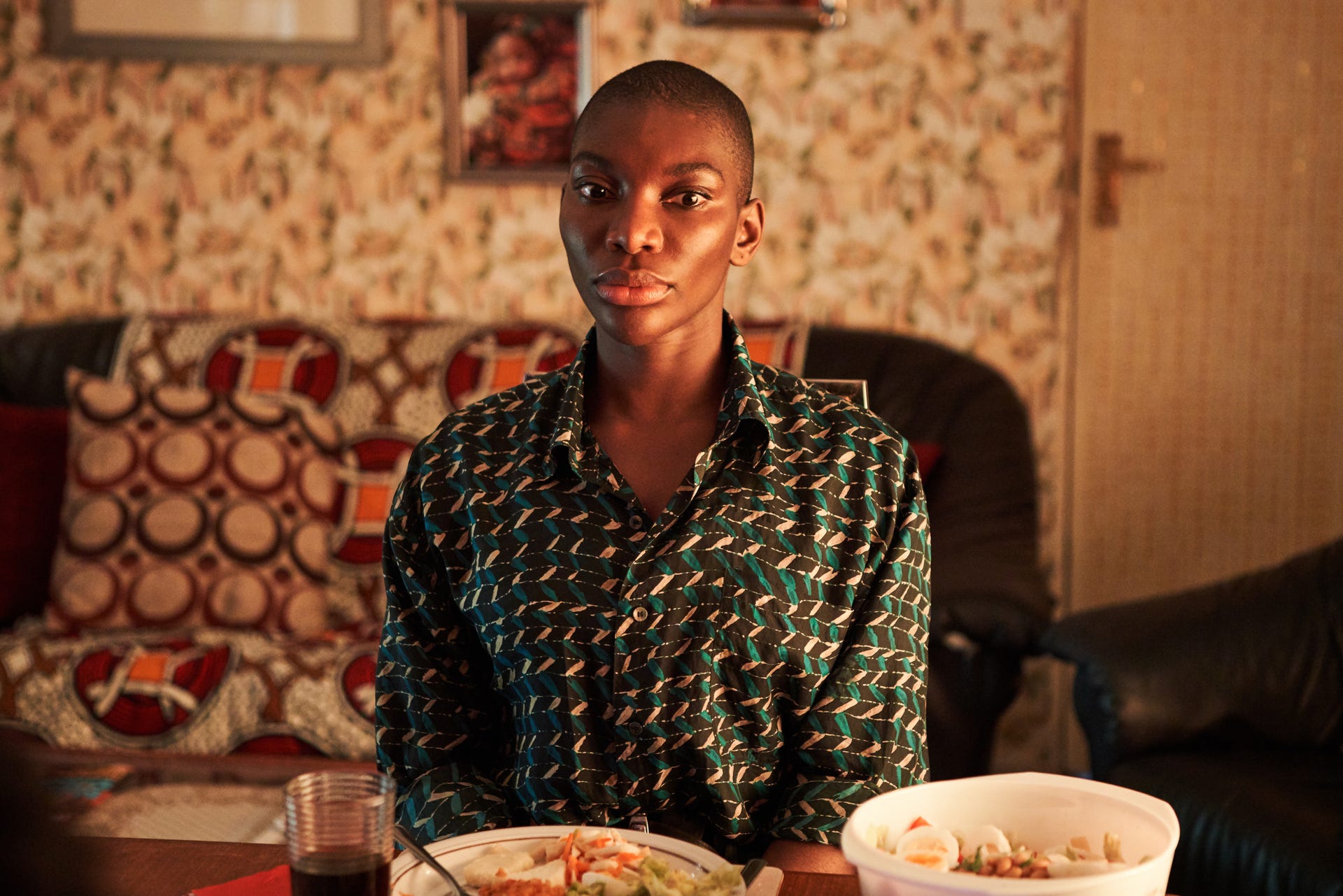 Arabella sitting at table in patterned shirt against patterned background.