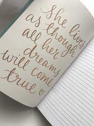 An open journal with the quote “she lives as though all her dreams will come true” on one side and lined paper on the other