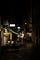 A nighttime alley lined with awnings of stores and cafes. Down the middle of the alley, one waitress with hand on hip.