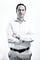 A man in business standing in front of a white background with his arms crossed.