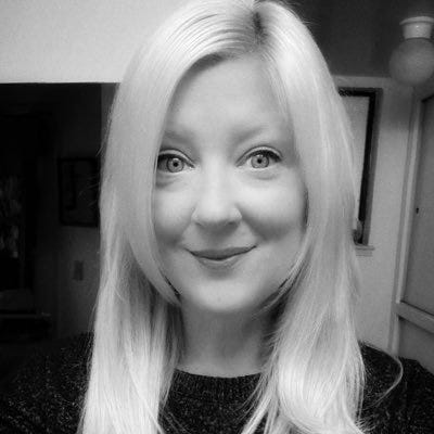 A black and white bust picture of a woman with light, shoulder-length straight hair and light eyes, smiling at the camera.