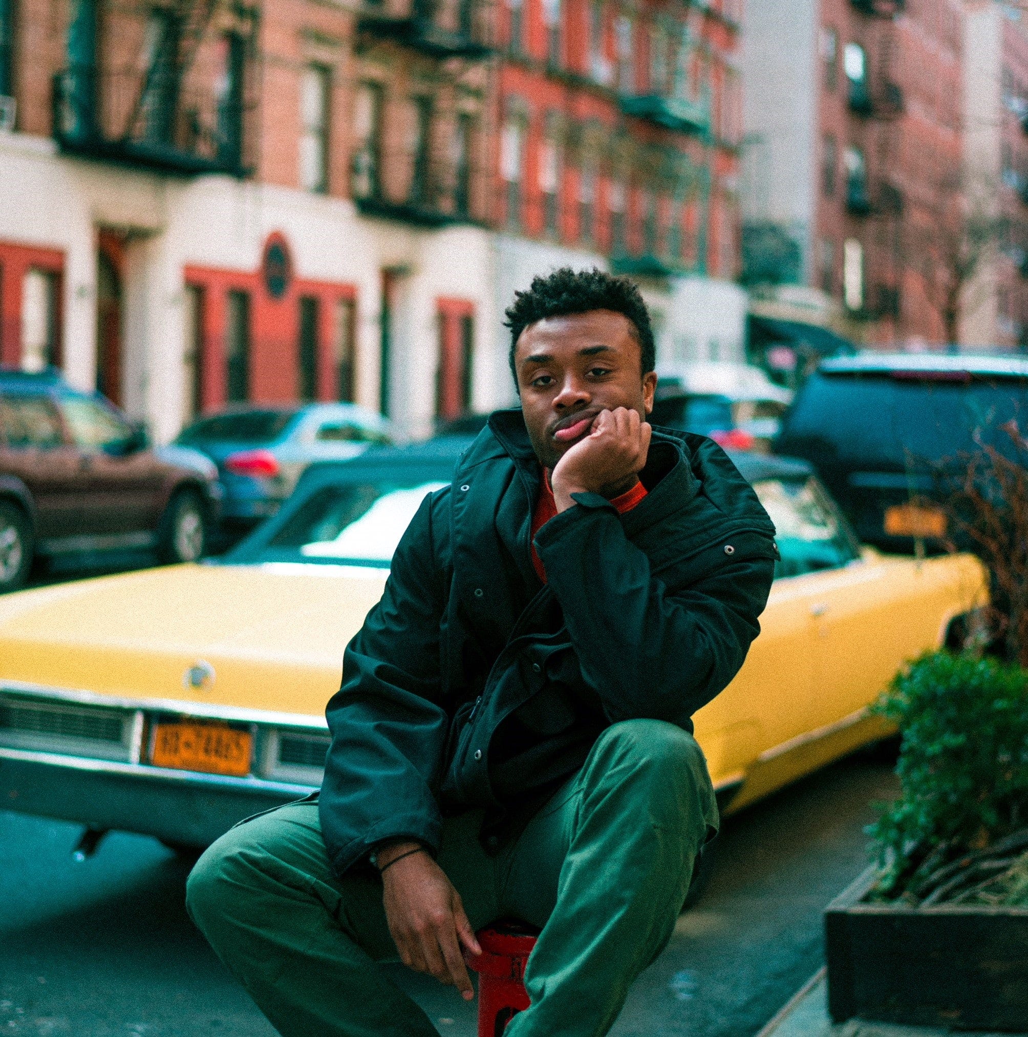 man sitting slumped with head on hand, in front of a yellow car