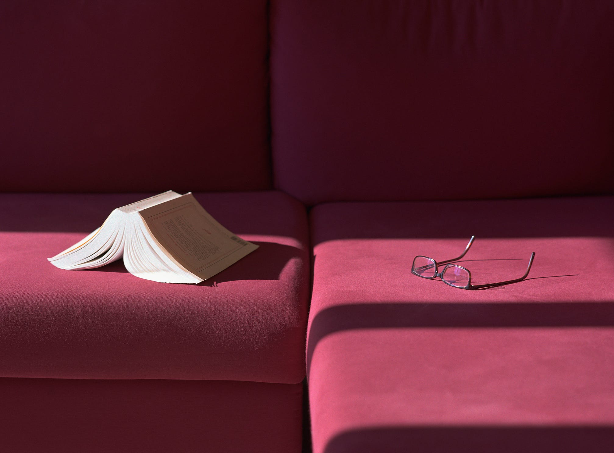 Book and eyeglasses left on a maroon velvet couch.