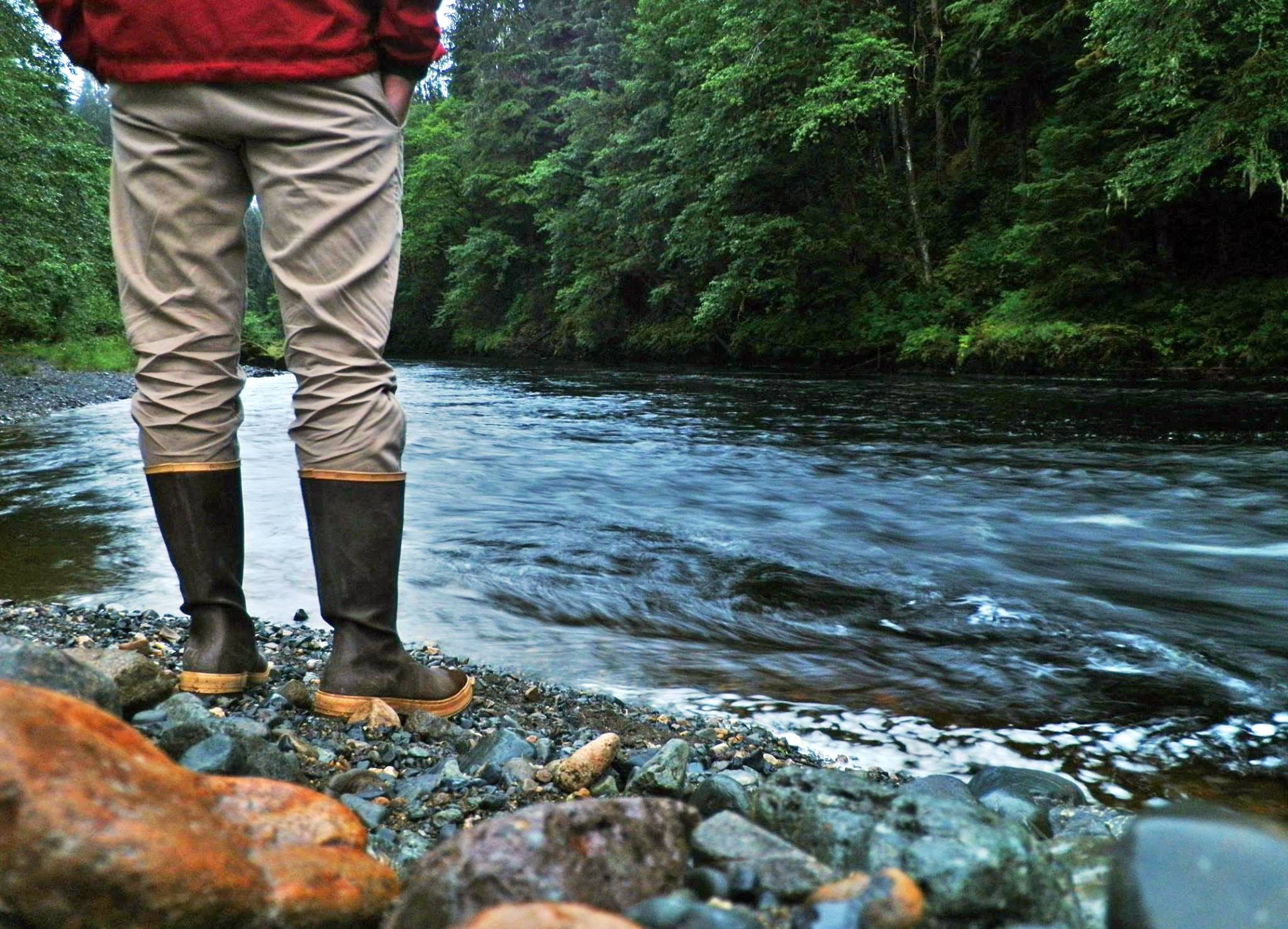 a man stands by a river bank in boots
