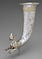 A large silver drinking horn with gold embellishments. There is a hole in the bottom of the horn, and the sculpted figure of a snarling cat garlanded with grape vines.