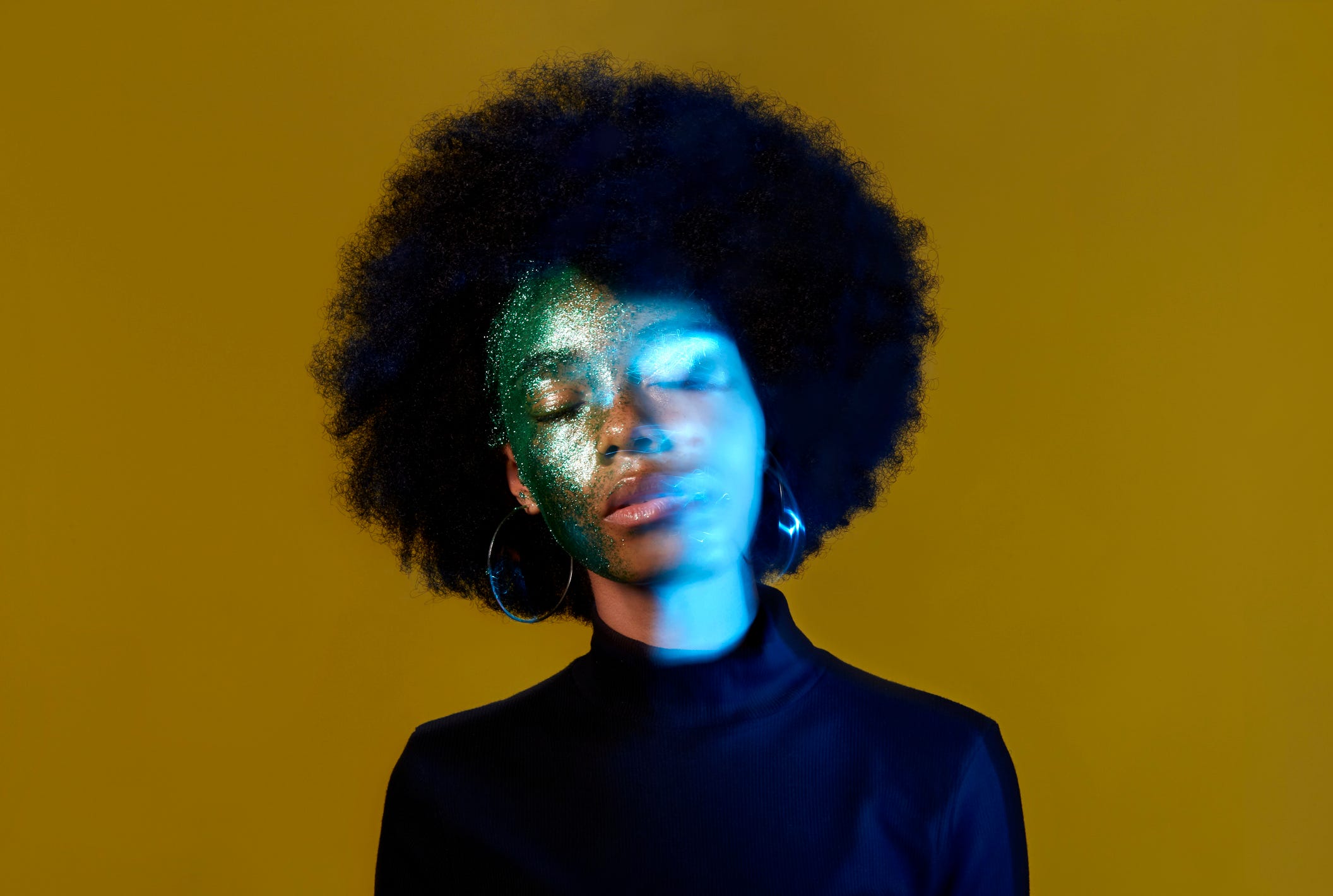 A conceptual portrait of a black woman with glitter on her face, with her face slightly blurred/double exposed.