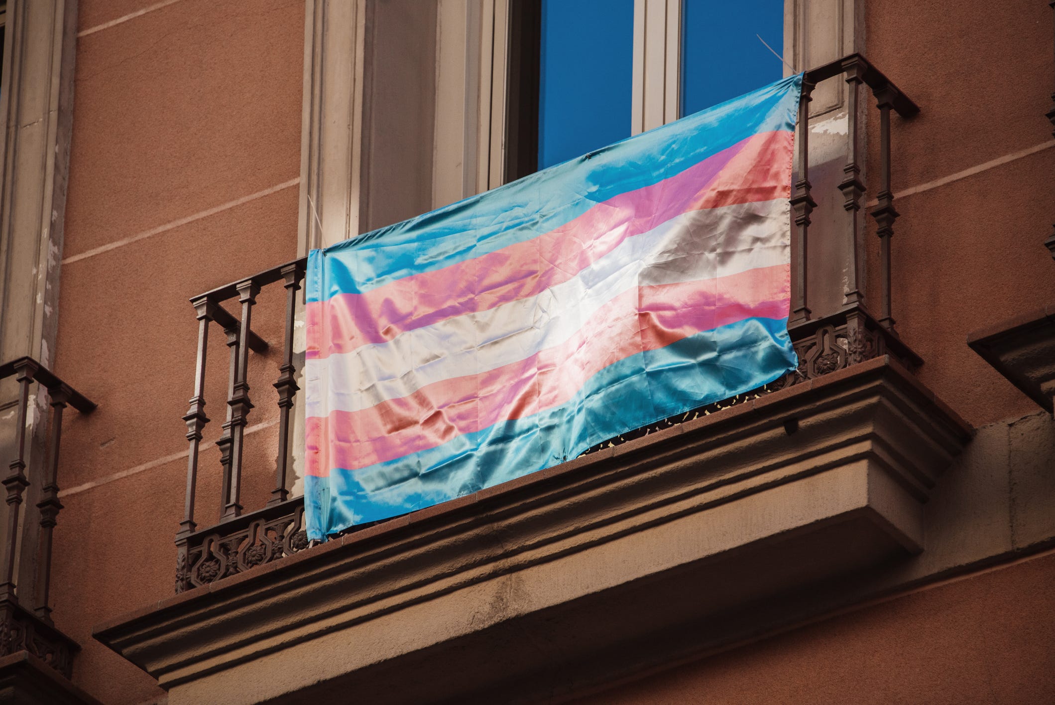 A photo of the trans flag hanging on a balcony.