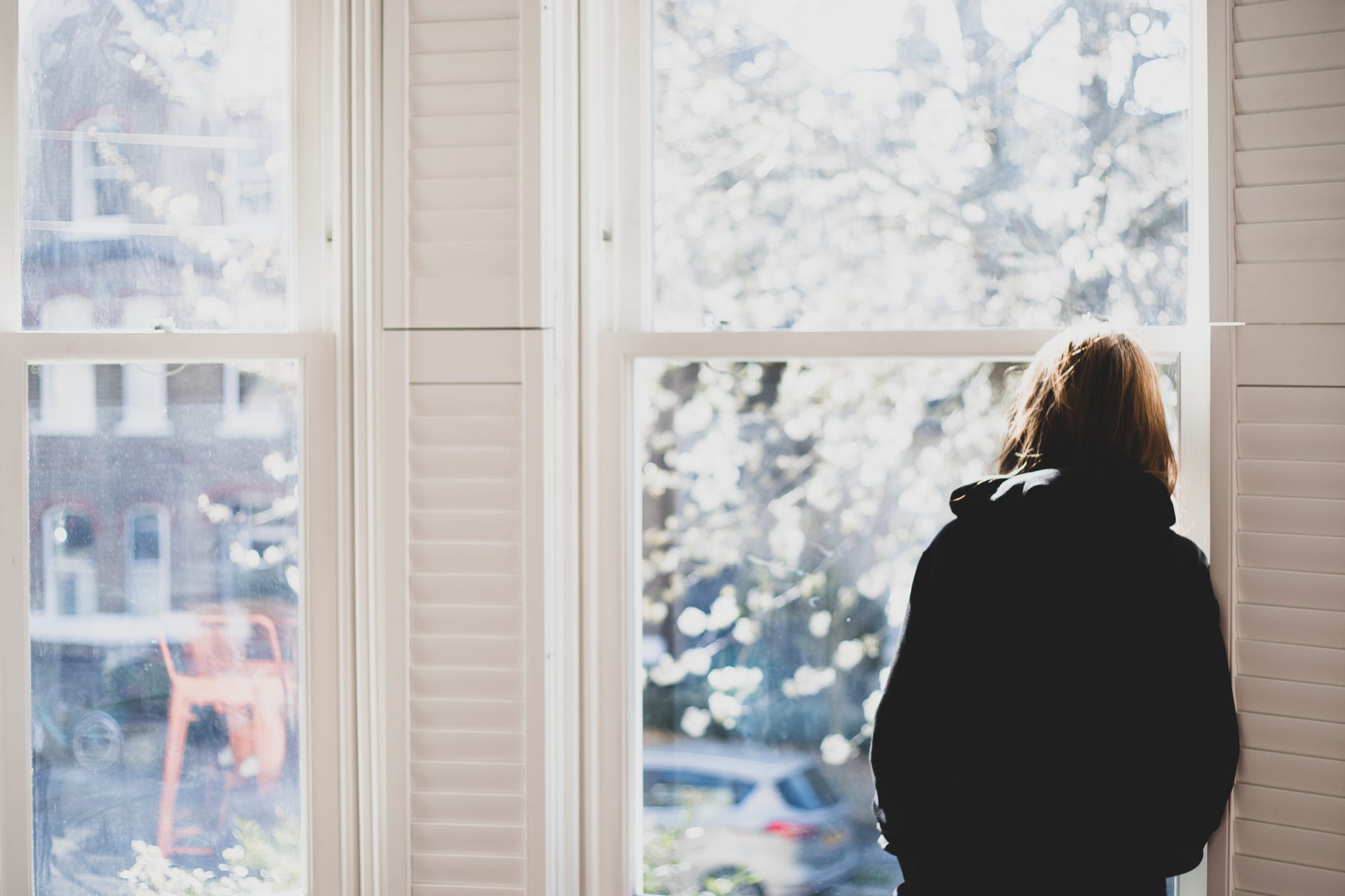 Rearview of a woman looking out a window forlornly.