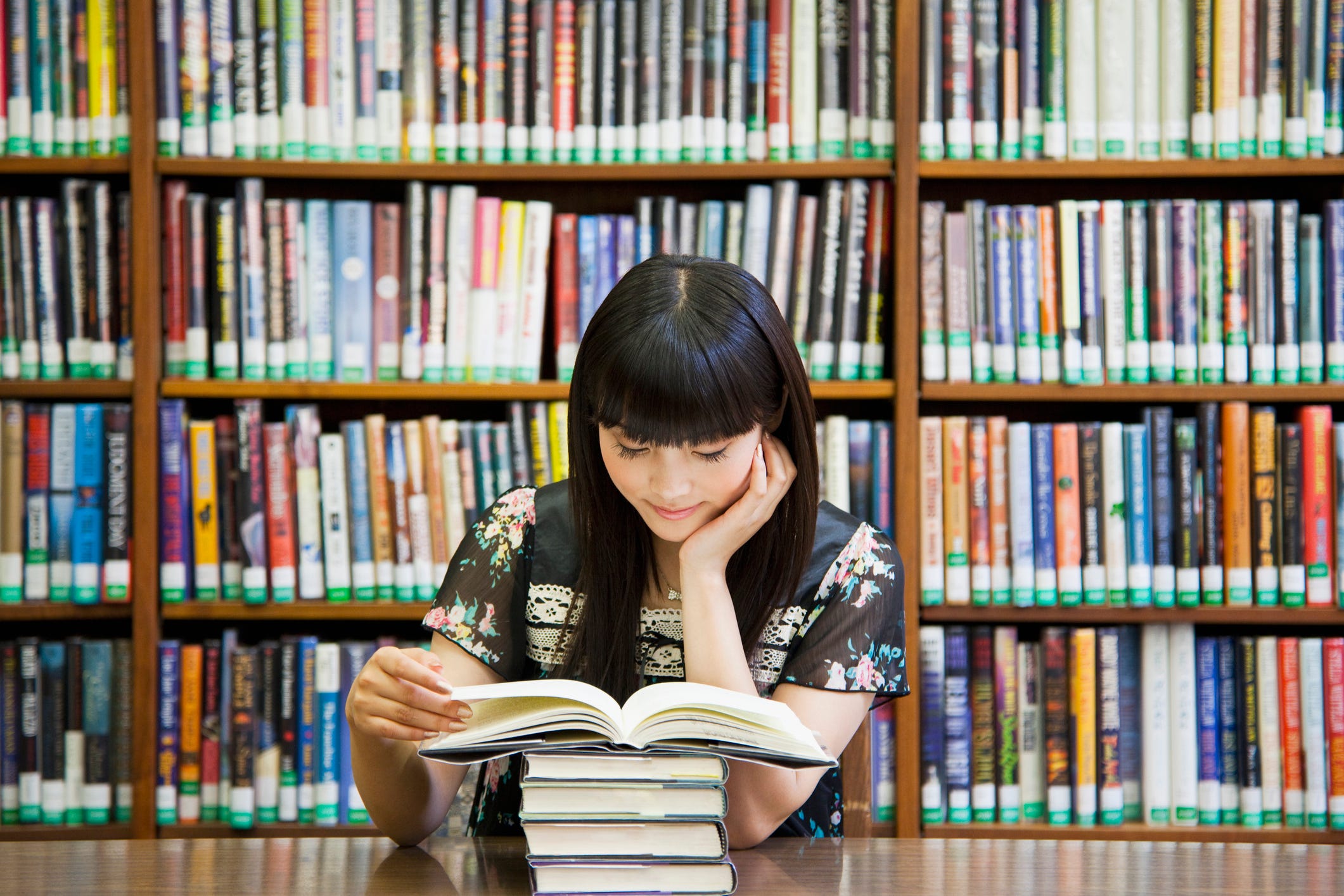 A photo of an Asian woman reading a book at a library.
