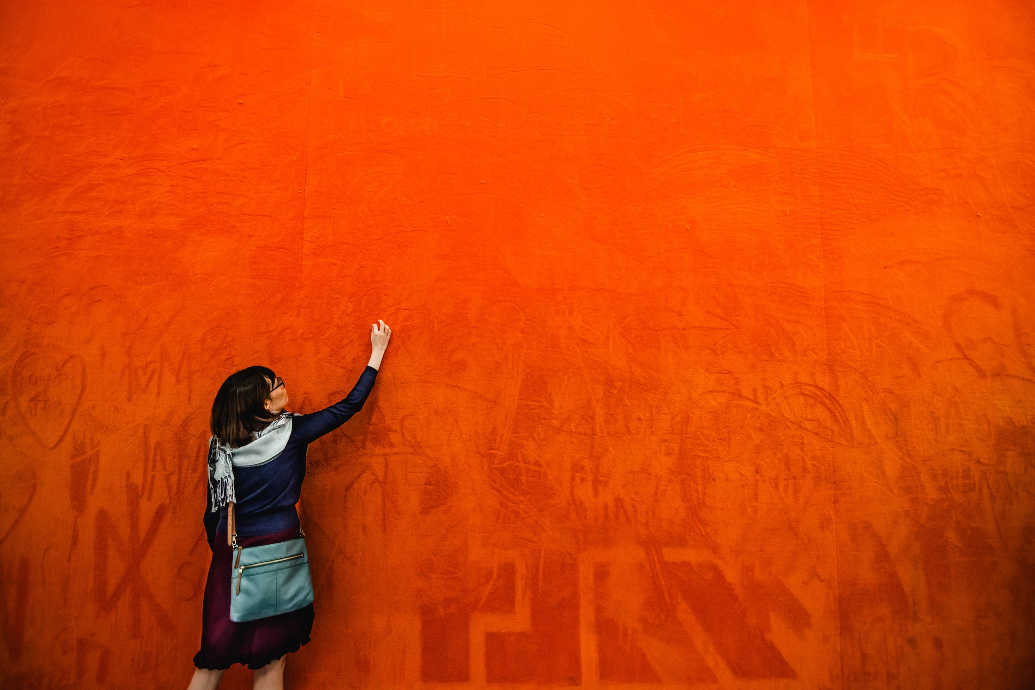 Woman writing on a bright orange wall.