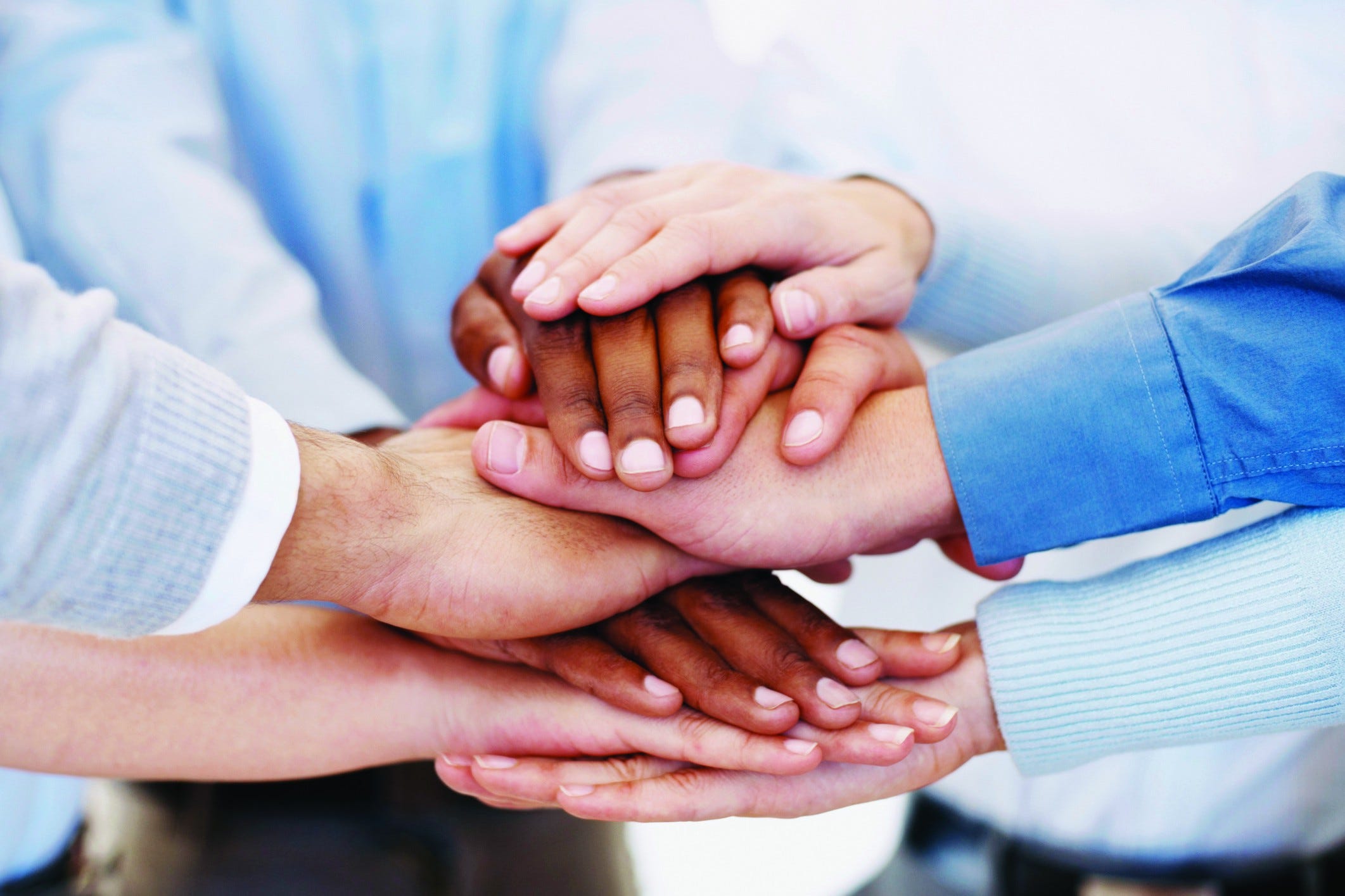 A series of different coloured human hands piled on top of each other, as to signify teamwork from a group of people