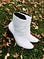 White ankle boots with a three inch heel placed on the grass surrounded by fall leaves.