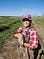 woman in red plaid shirt, camo pants and hat, sunglasses on hat holds a duck