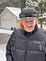Older gentleman dressed in a winter coat and felt hat standing in front of a garage in the snow.