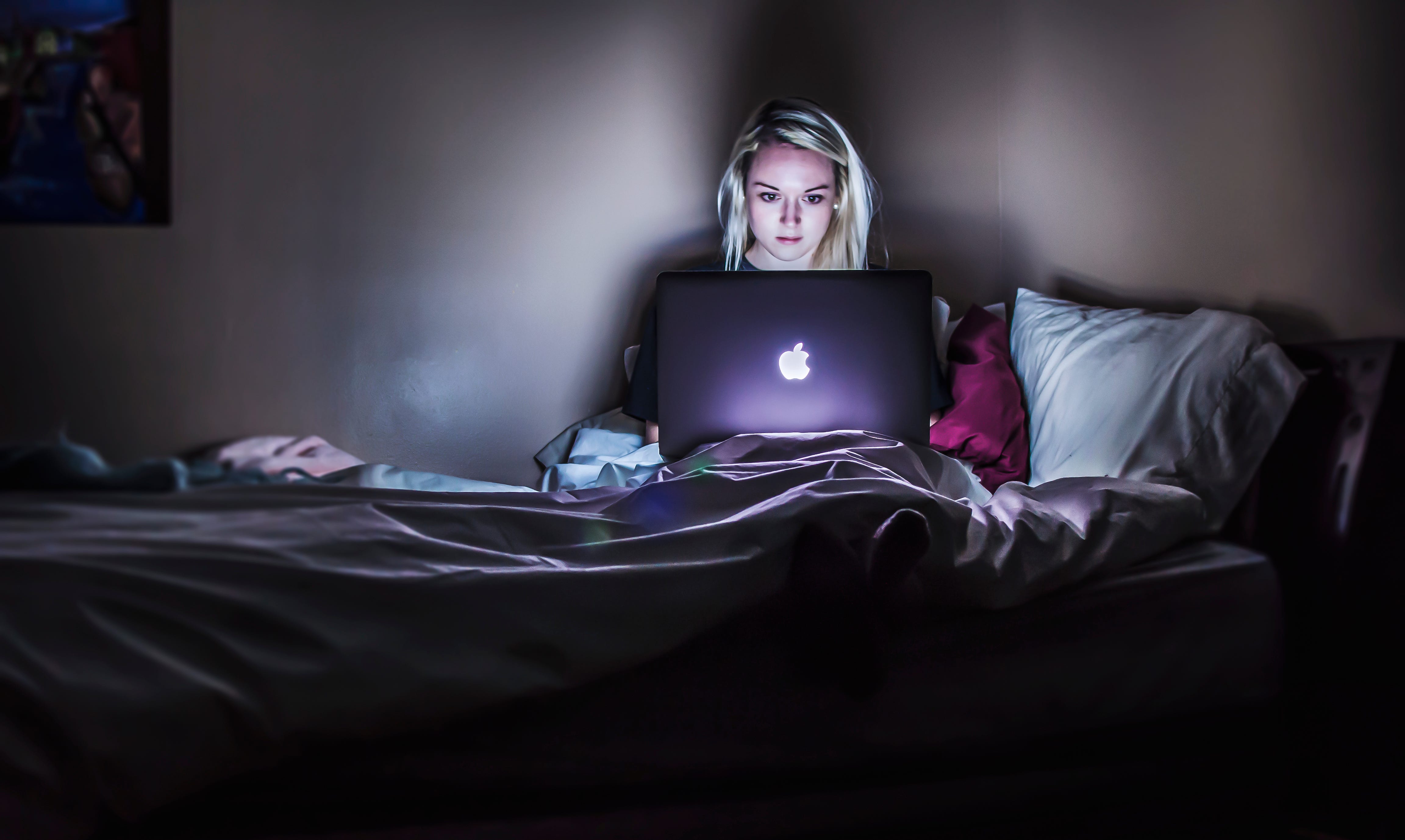 Young woman in bed with open laptop illuminating her face