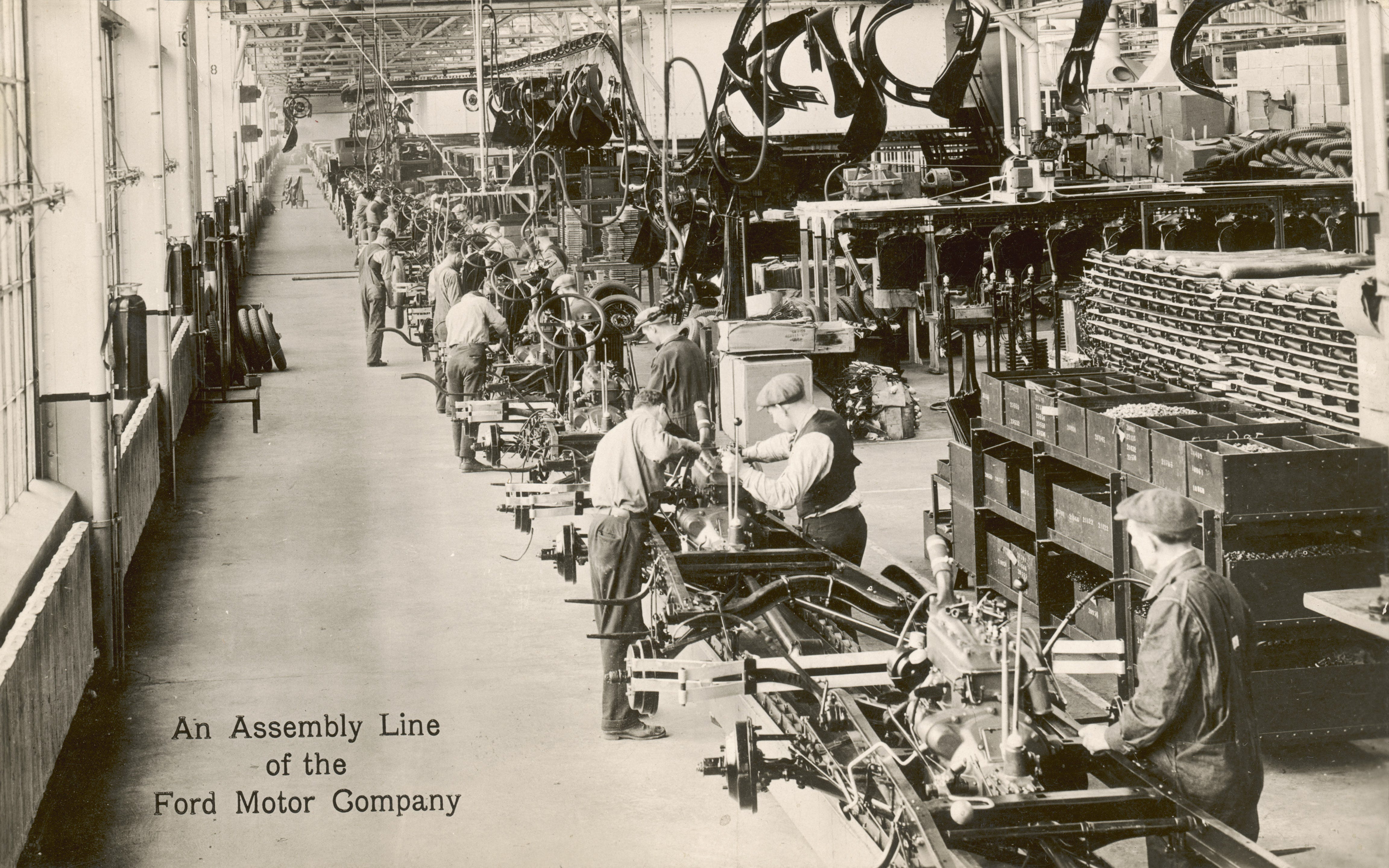 Sepia photograph of a Ford assembly line from the early Twentieth Century.