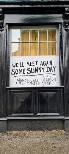 A sign in a pub window reading “We’ll Meet Again Some Sunny Day”, with graffiti