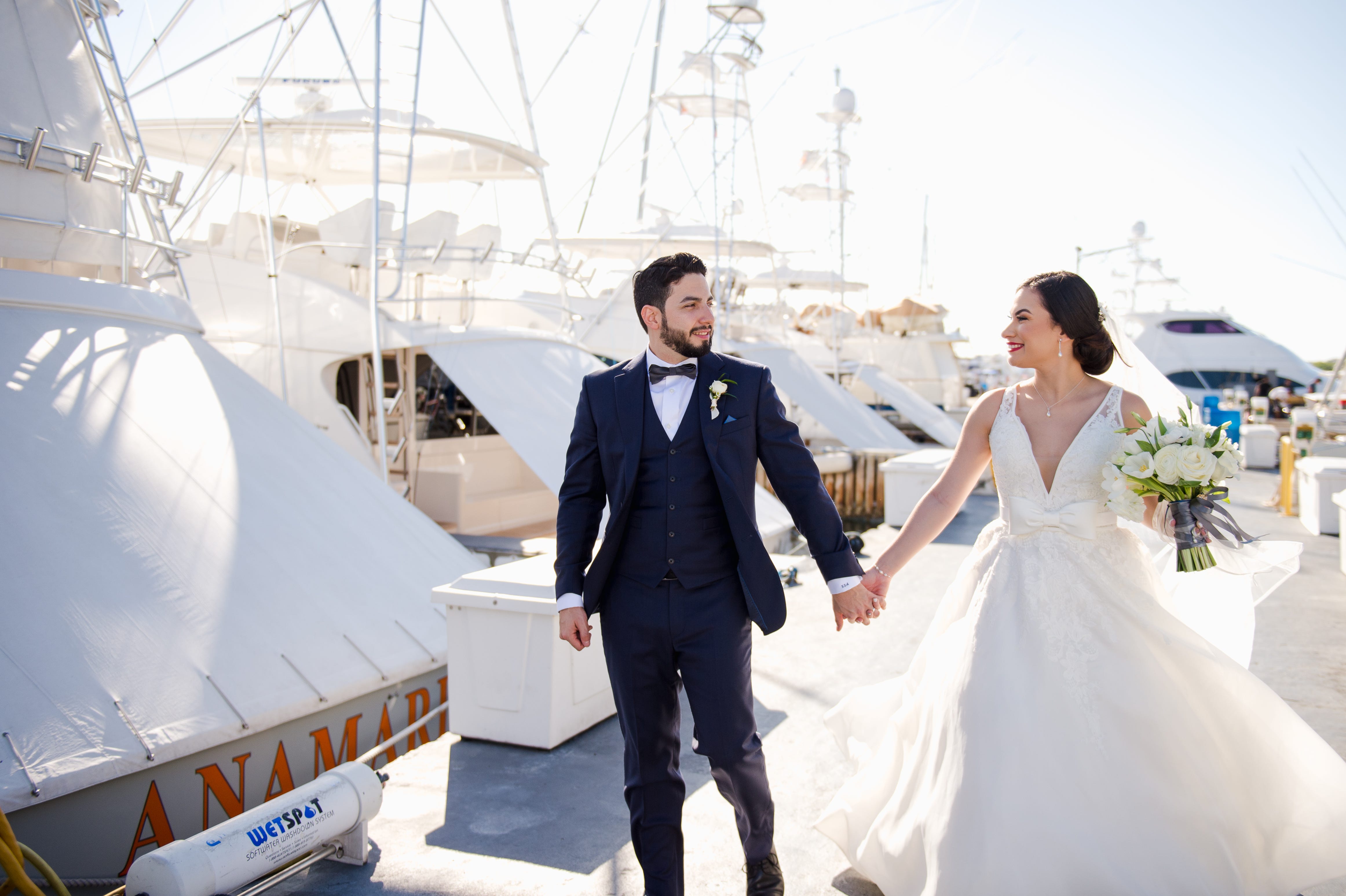 Bride and groom walking over a pier with boats around.