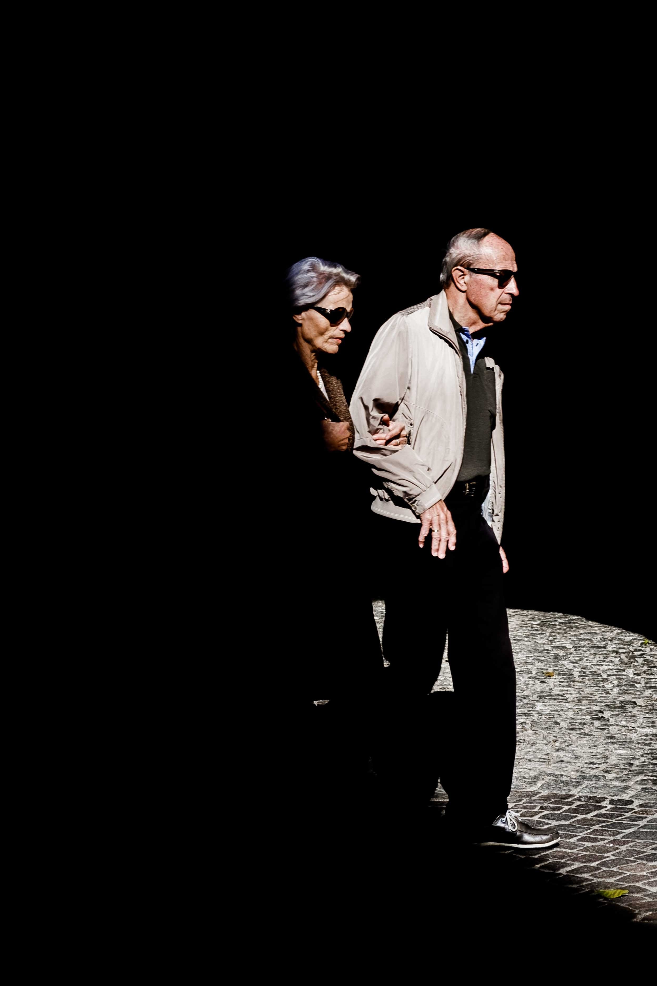 Man and woman linking arms and wearing sunglasses walking down the street