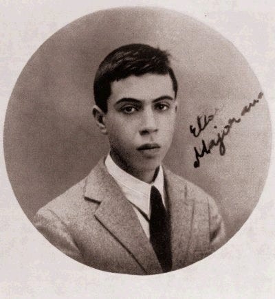 Sepia photograph of a young man with dark hair and eyes, dtressed in a suit. The words "Ettore Majorana" are written diagonally on the photo in tiny handwriting