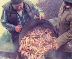 two men dumping a bucket of hooligan into a pit