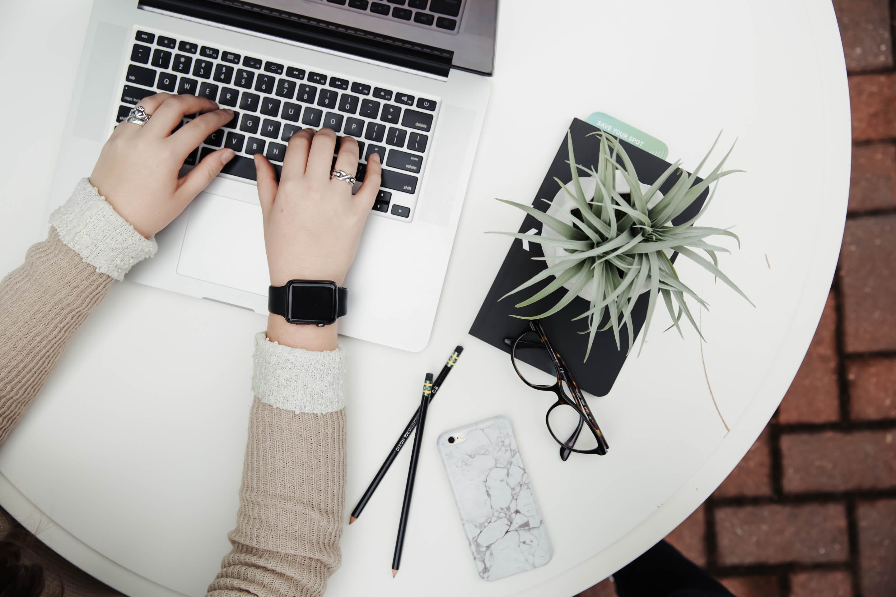 round white minimalist table with notepad, plant, pencil and woman's hands typing on laptop