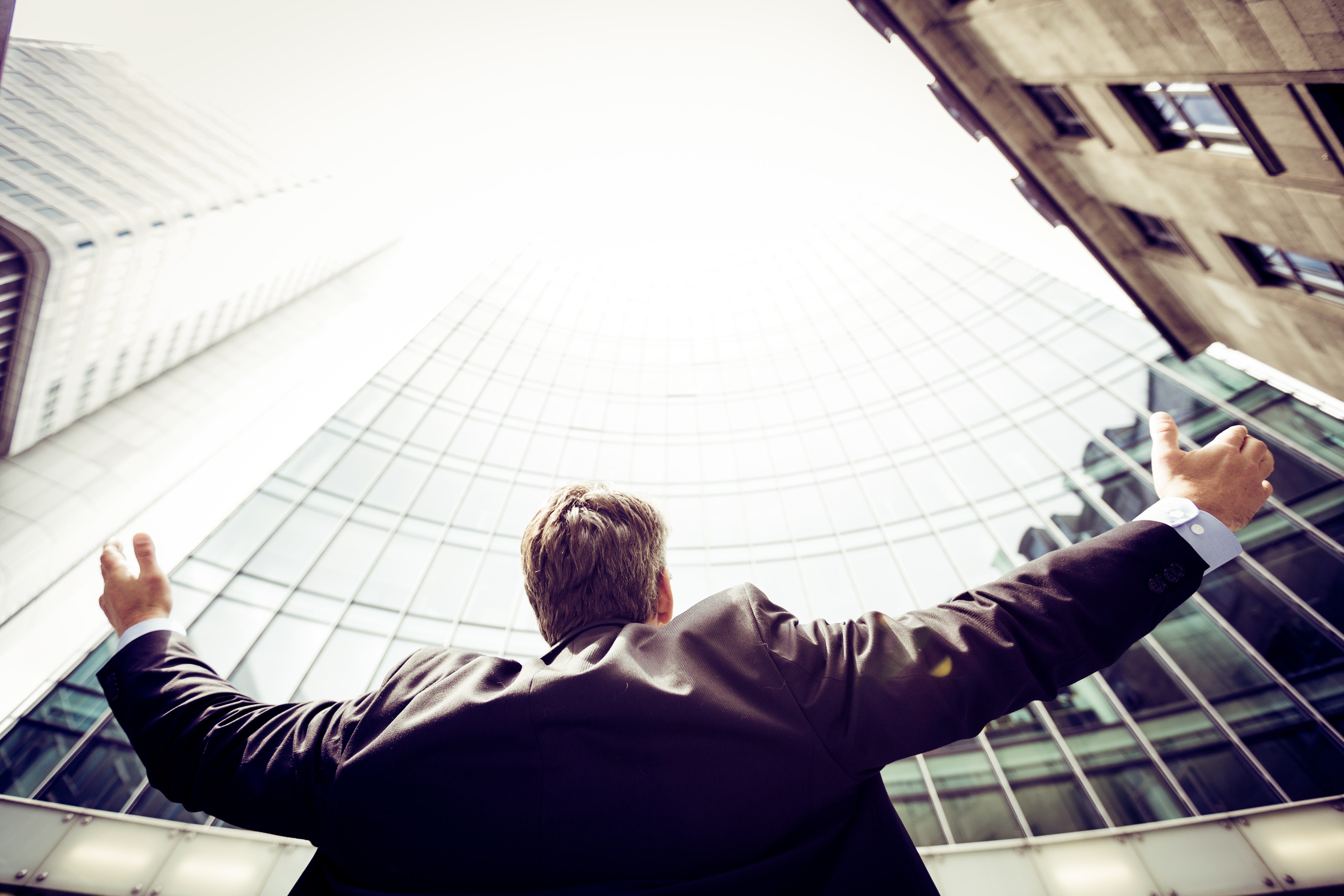 Business man looking up at skyscrapers with arms open