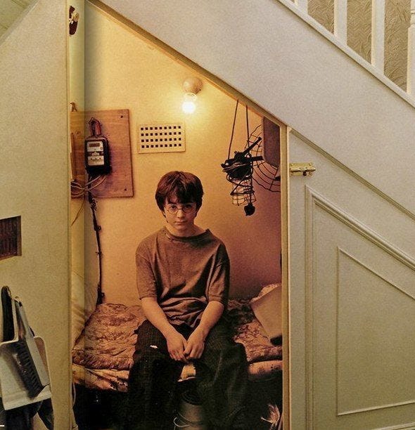 Photo of Daniel Radcliffe as Harry Potter sitting on a bed in a cupboard under the stairs.