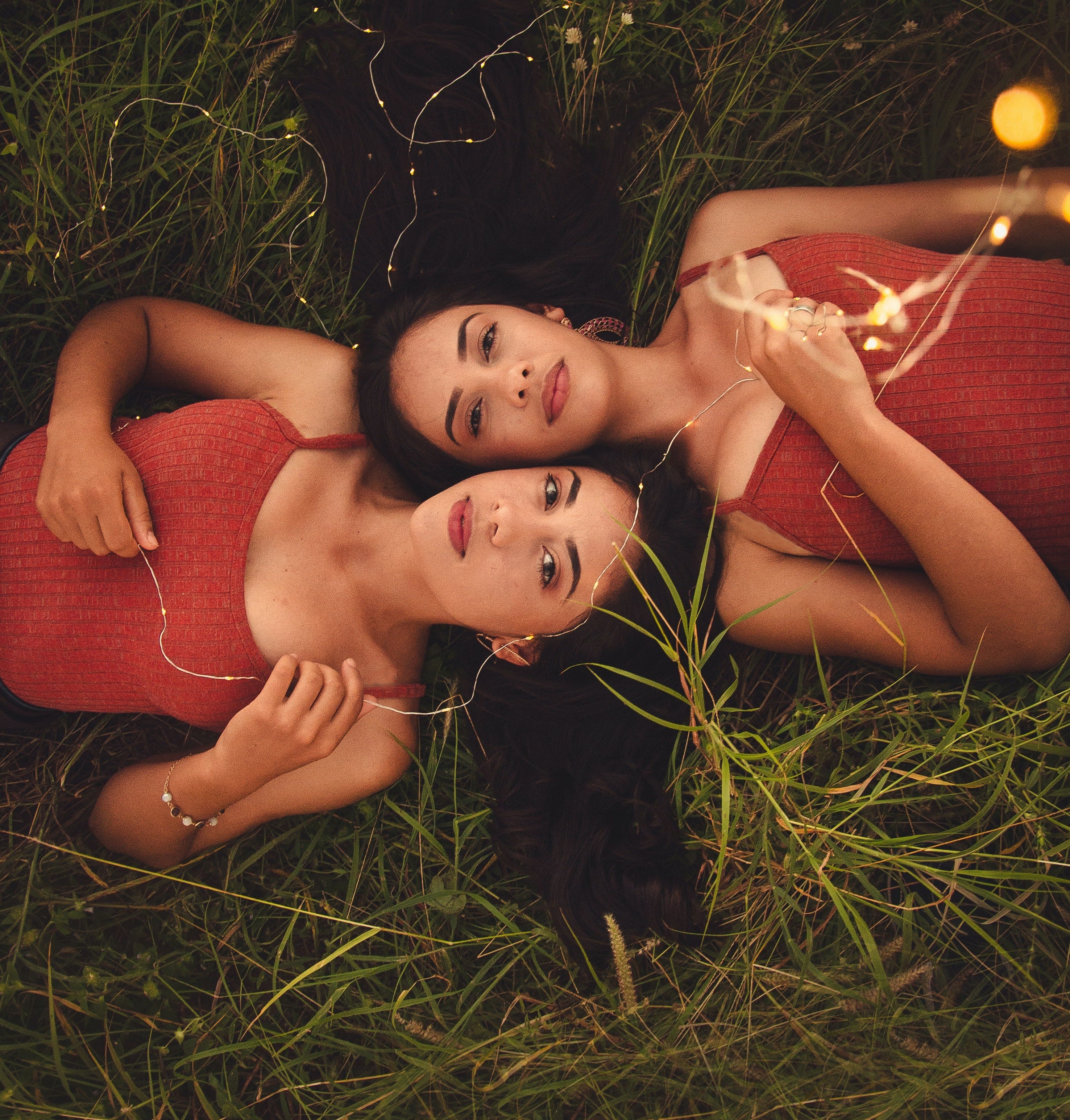 Two sisters laying on the grass next to each other.