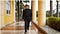 Dr. Herbert Wertheim with his signature red fedora walking by a beautiful yellow building in Florida.