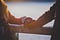 Cropped photo two arms & torsos wearing winter clothing, with the hands touching while resting on top of a railing.