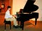 Luke Brenneman, in contrast to running photos is show in a dress shirt and slacks, seated and playing a grand piano.