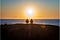 A couple sitting at the oceanfront, watching the sun setting over the water.
