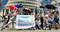 Kiwi Bottle Drive campaigns stand outside the Beehive with a banner that says, Support Bottle Deposits. Many of them are hold