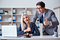 Professional man and woman in business suits with fake smiles at desk with laptop and gavel on it.