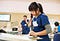 A photo of a clinical setting with three people in scrubs doing administration. In the foreground a nurse is on the phone.