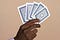 A closeup of a Black person’s hand holding four playing cards with their backs to the viewer.