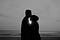 Silhouetted man and woman standing before the ocean in black and gray.