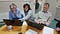 shows a man in the centre of three people looking at two laptops