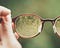 A person is holding a pair of glasses, bringing an image of a tree into focus.