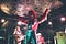 Orville Peck in a red, fringed western costume raises his hand at a live concert.